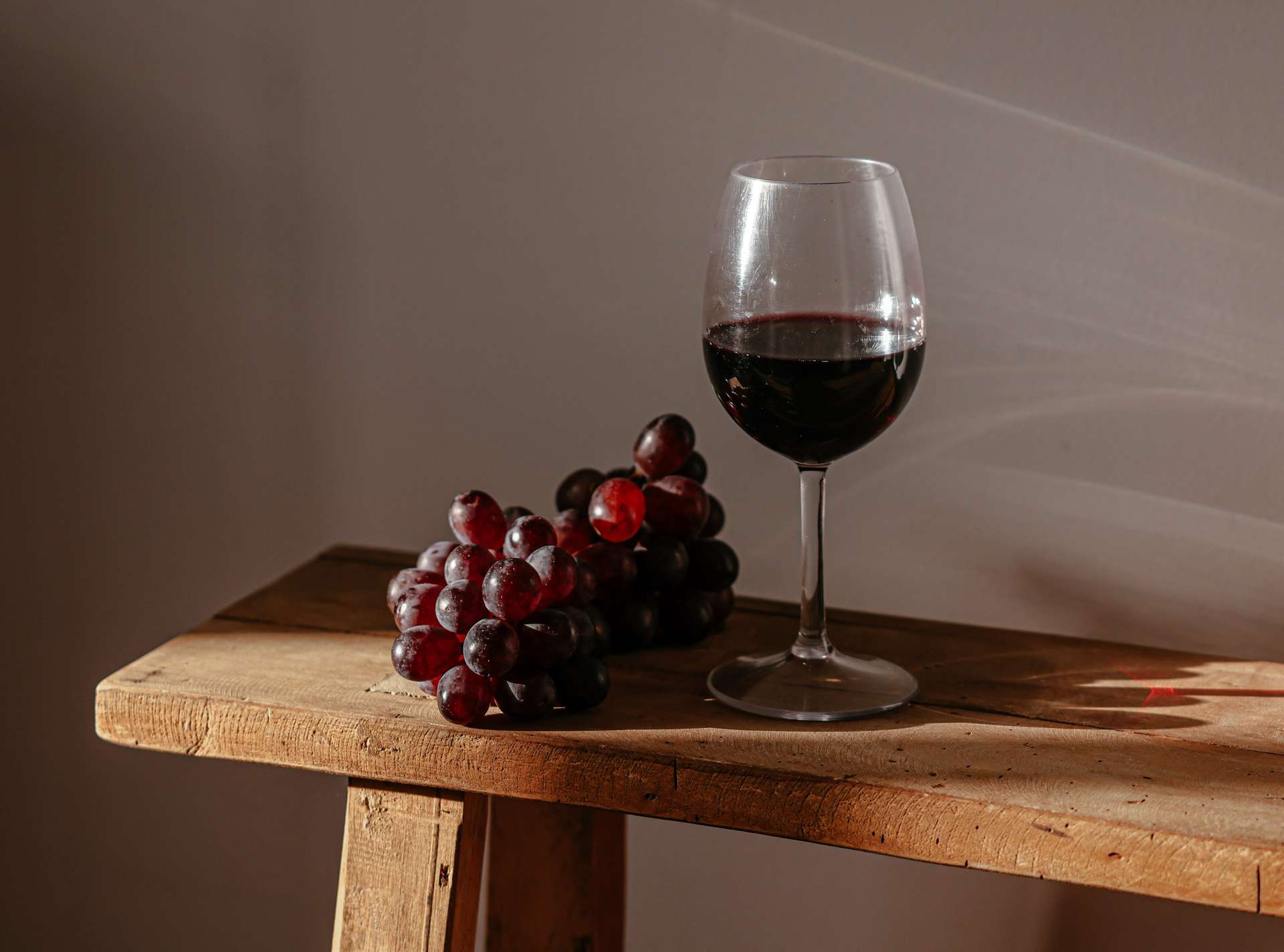 a glass of red wine and bunch of black grapes on a wooden bench